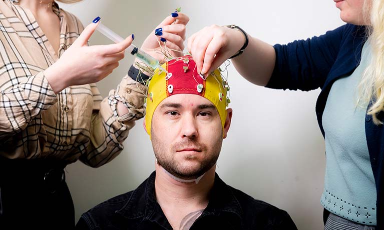 student wearing a cap with electrodes attached and 2 students checking them