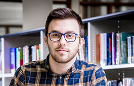 male student sitting in front of a shelf of books
