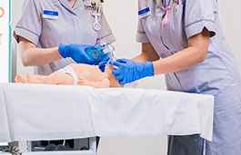 Two nurses putting a breathing mask on a doll lying on a hospital bed 