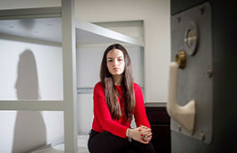 Female sat on a bunk bed inside a cell with the door slightly open