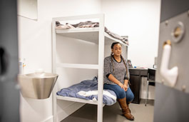 A lady sits on a bunk bed in a prison.