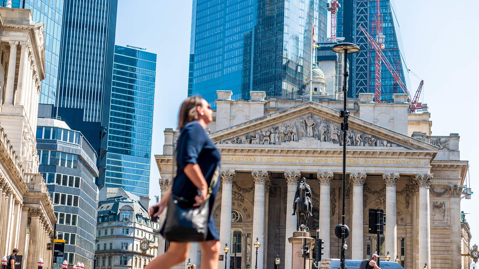 A woman walking in front of the London Exchange.