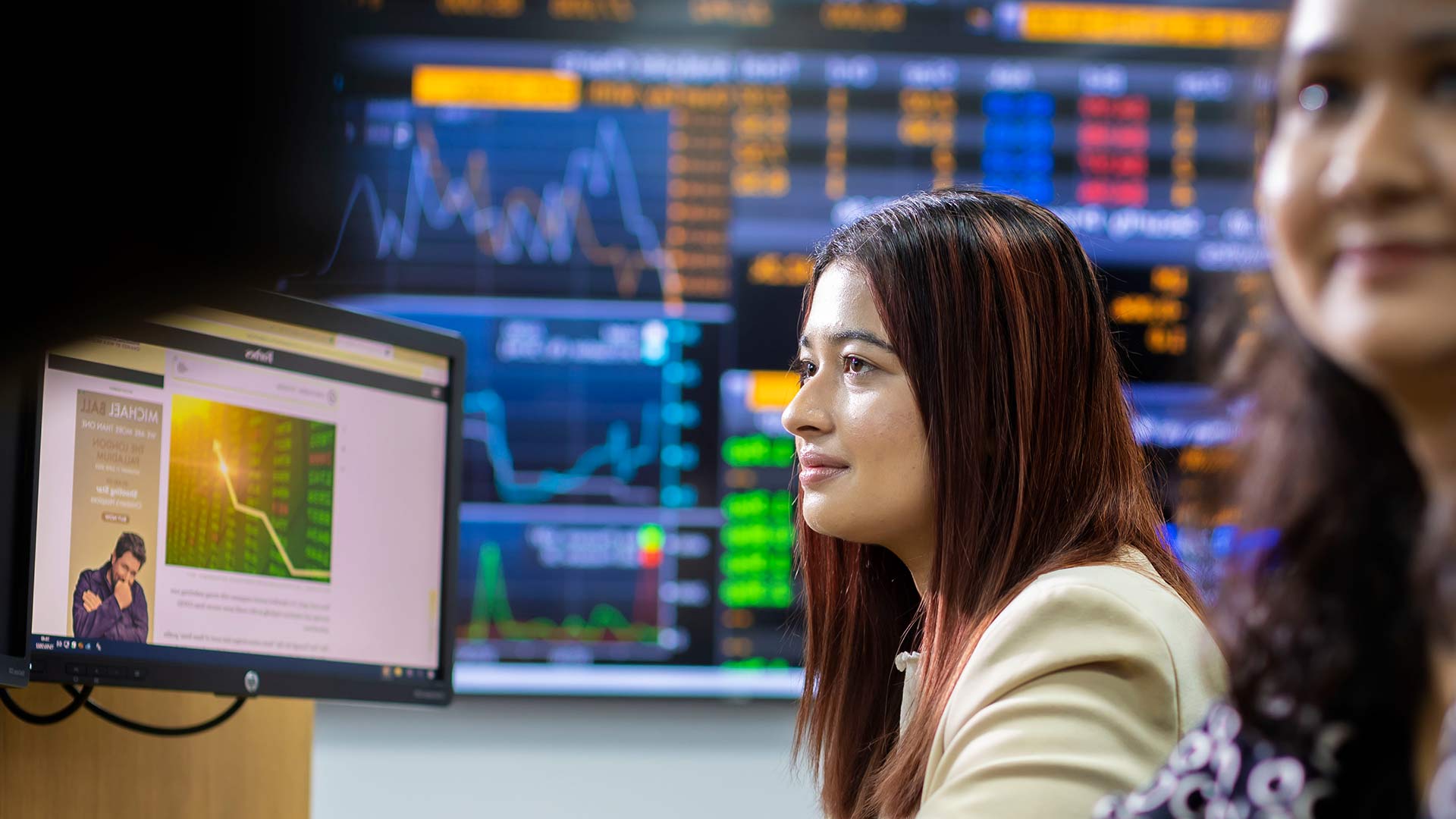 Adult female wearing a beige jacket looking at a monitor displaying a graph