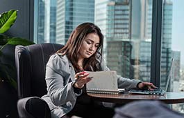 Female student in smart dress sitting at a desk looking at a notebook and laptop hair looking at a tablet
