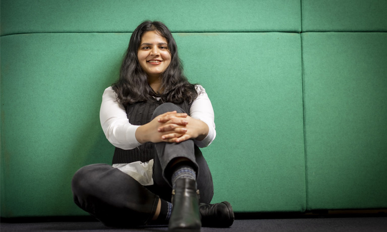 Eshita sat on the floor smiling, against a green background