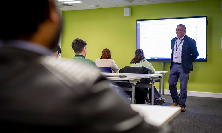 Classroom with green walls and students sitting at their desks while a teacher gives a lecture