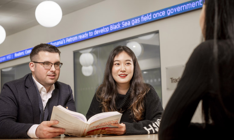 Two students with a textbook on the Trading Floor