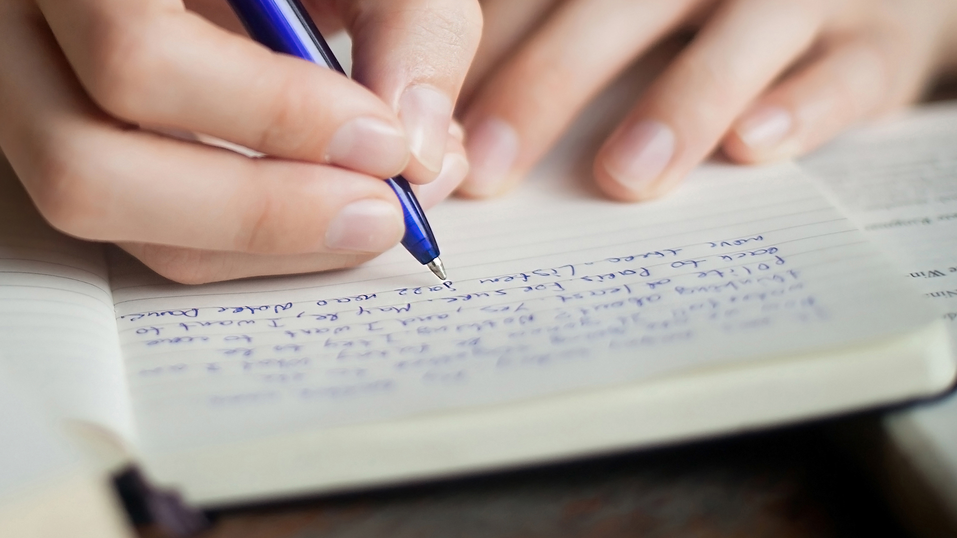 Close up of a hand holding a blue pen writing in a notebook