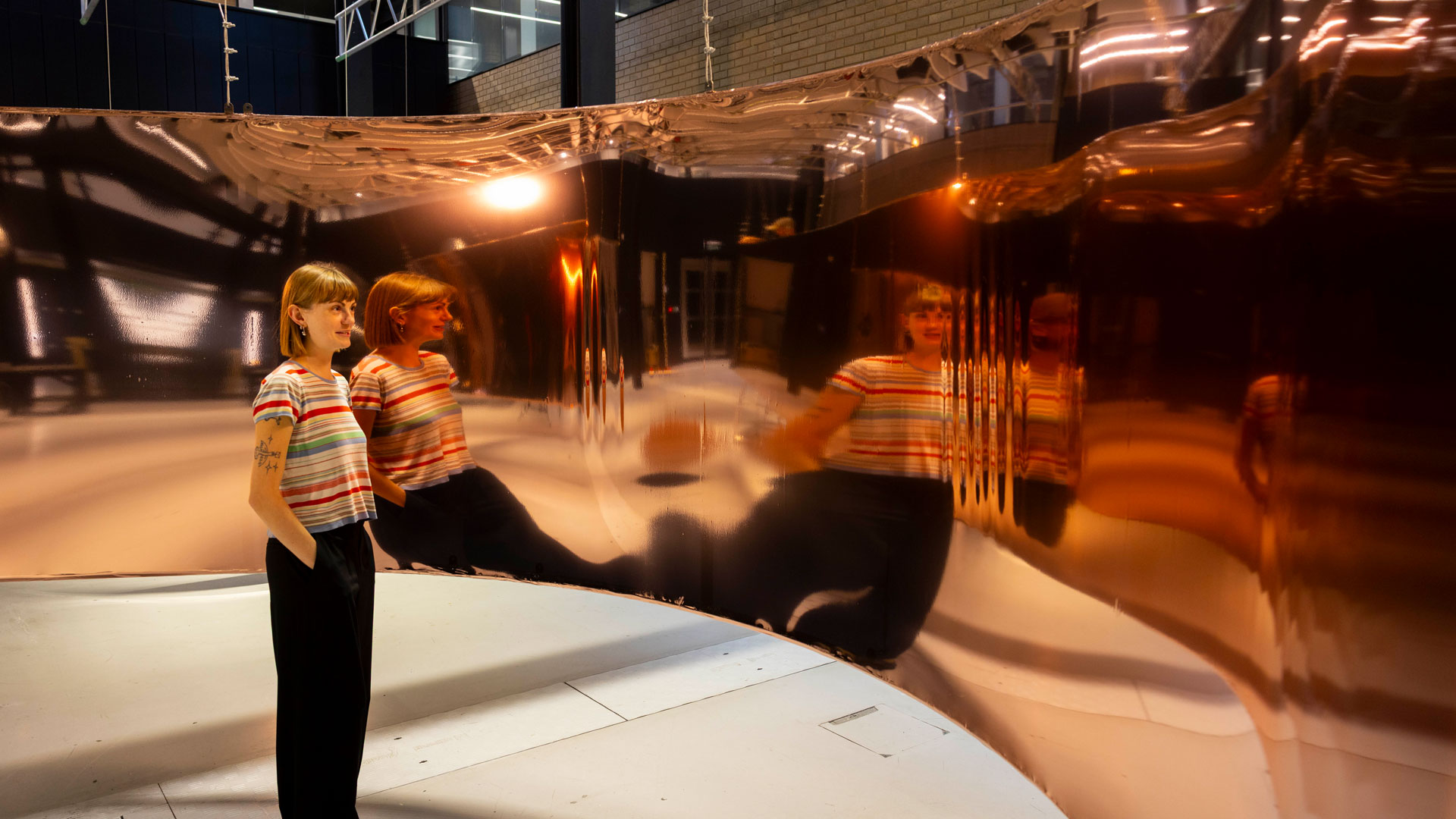 A British Art Show 10 installation showing the artist stood in front of a burnished sheet of reflective curved metal