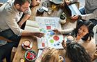 Aerial view of a small group of people sitting around a table looking at a colourful diagram