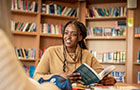 Female sat at desk reading a book in the library.