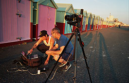 Two men looking at a laptop next to a camera on a tripod