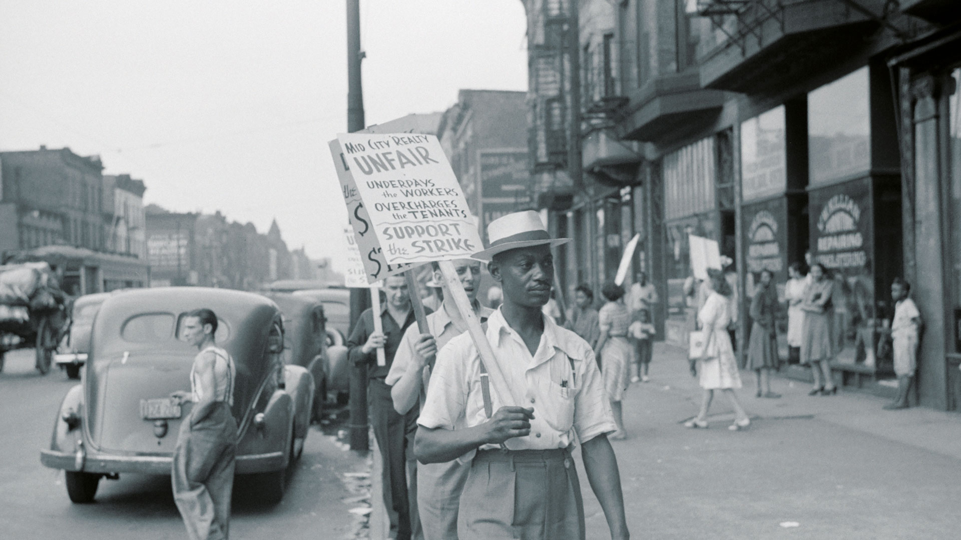 three men with picket boards walking down a street protesting with passers by in the background