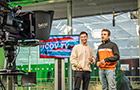 Two students sitting in front of a filming camera emulating a tv studio