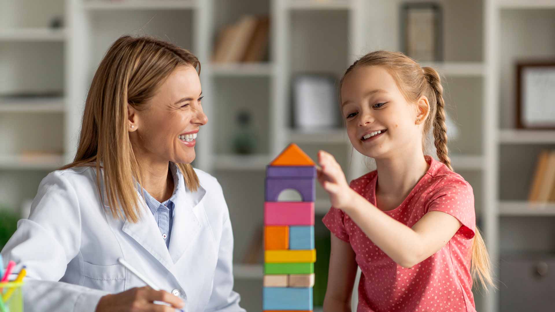 child playing with building blocks whilst a professional observes and smiles
