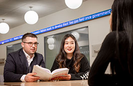 students holding a text book at a table in study area