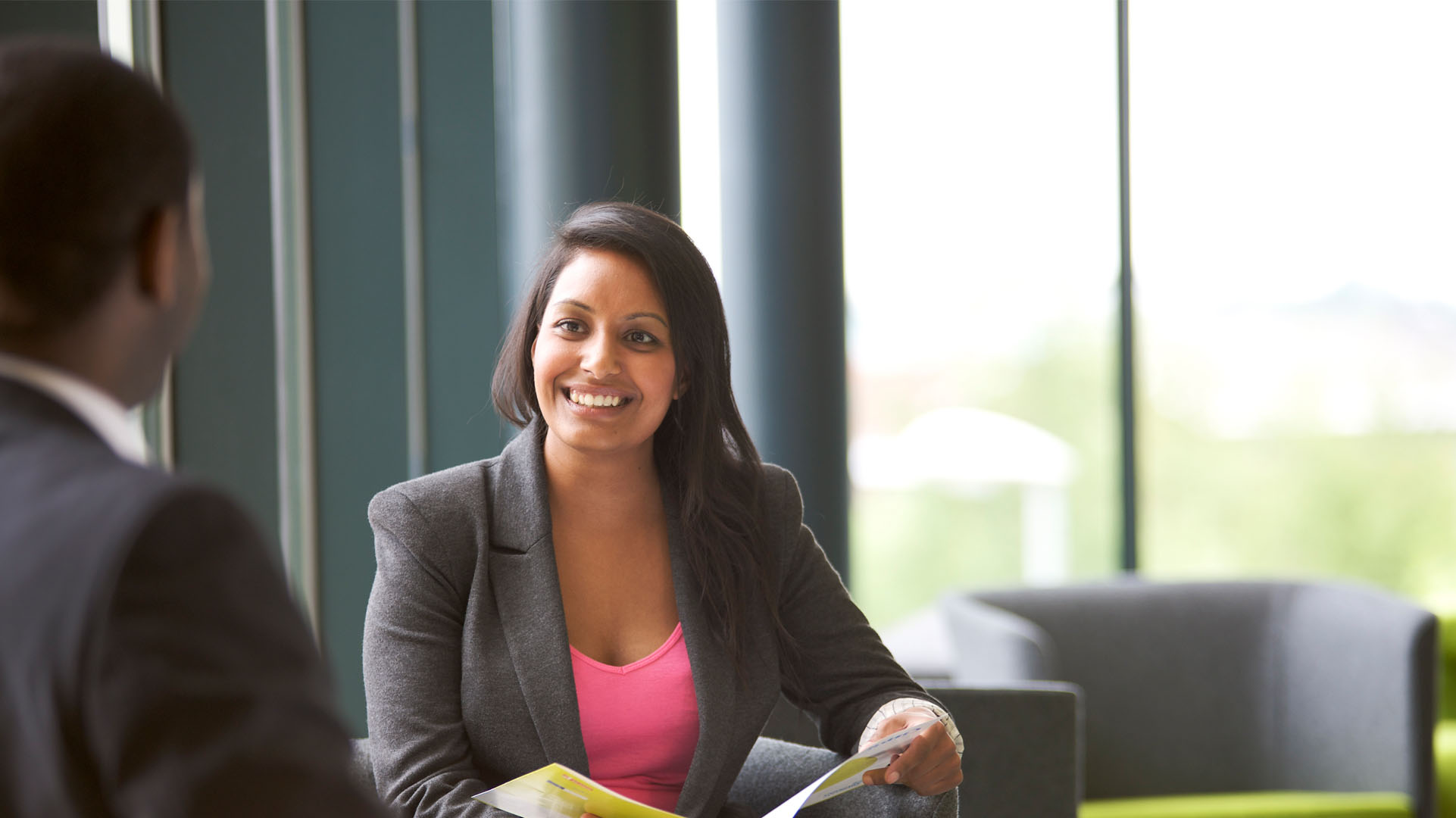 Young professional woman chatting to a man sitting at a table 