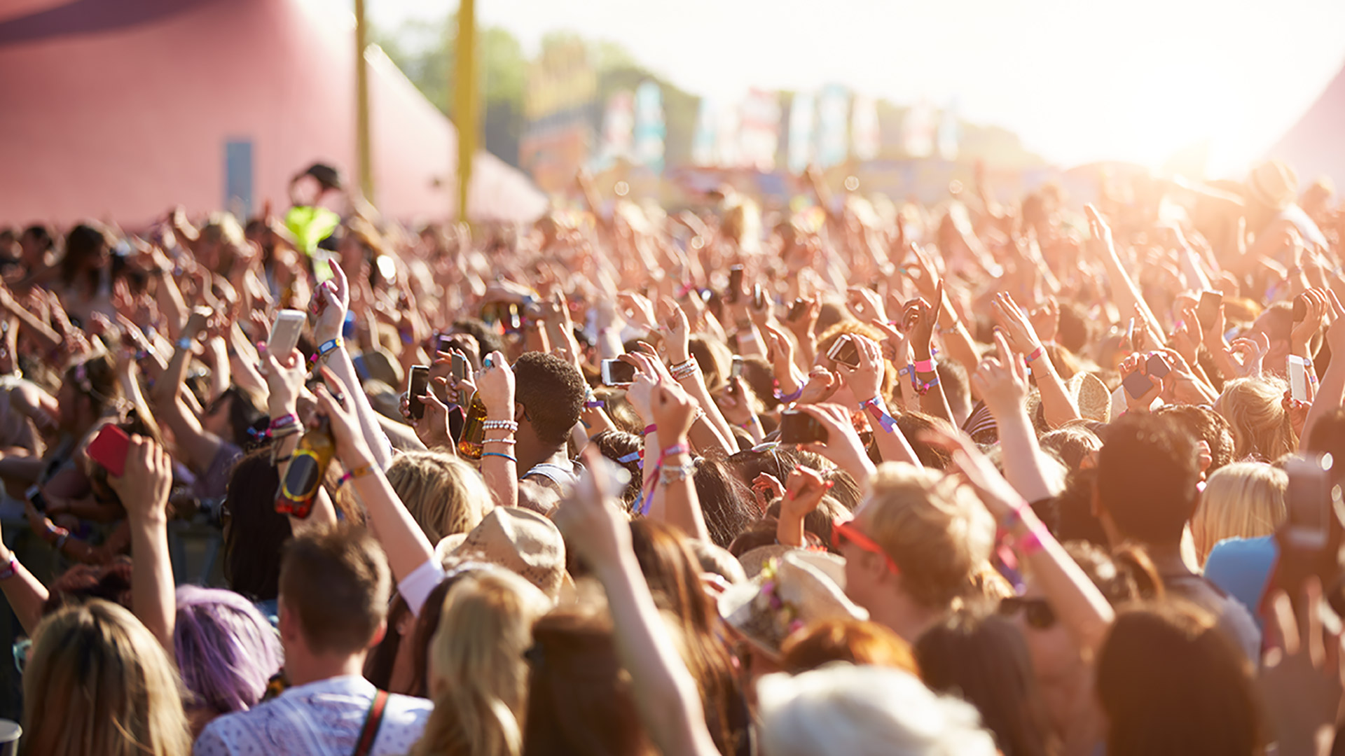 Large crowd at a concert with arms up facing the stage on a bright sunny evening