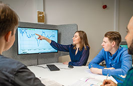 Student in a group pointing to a chart on a screen
