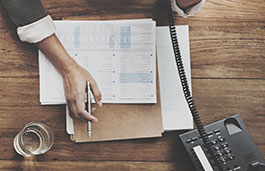 Desk with diary, notes, a glass of water and a person on the phone just out of shot