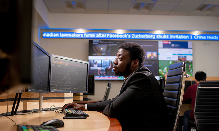 Student sitting at a desk looking at multiple screens with a ticker tape running in background