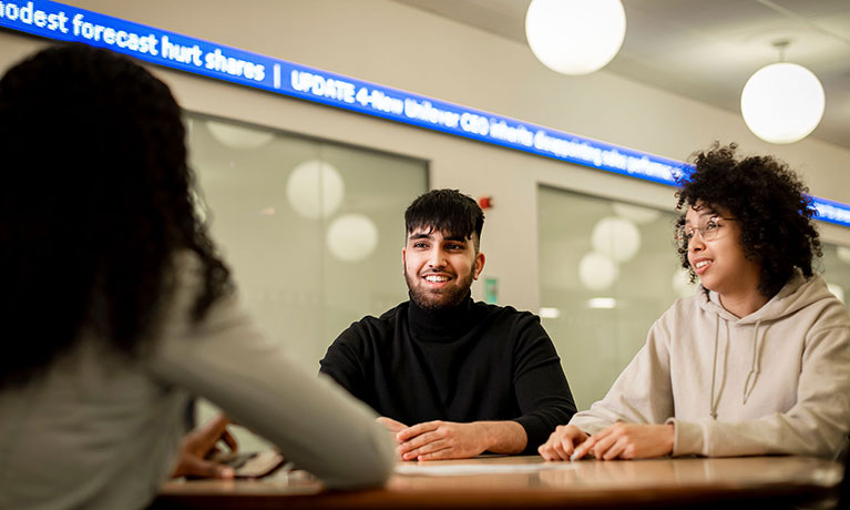 Three students talking, one facing away from camera and the other two smiling at her