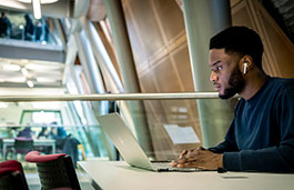 A student with earbuds in focuses intently on his laptop