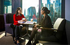 Two students sat round a table in front of a large window with the London skyline in the background