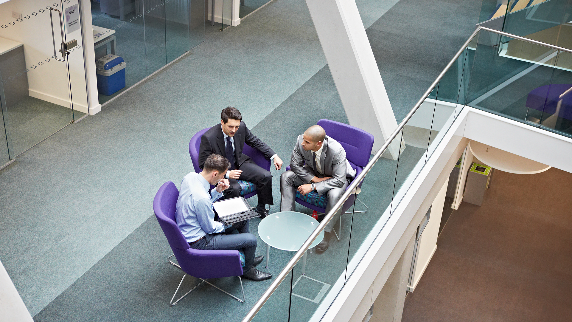 Down facing view of a group of three men wearing suits having a conversation at a table