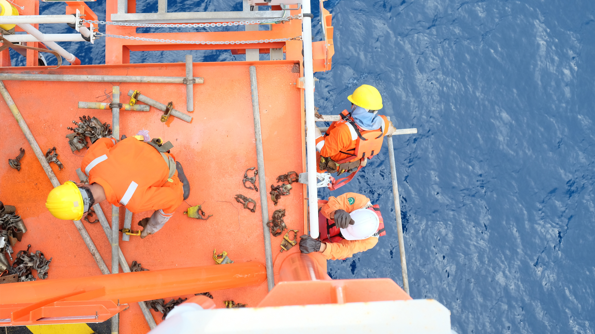 Three workers in construction gear on platform above water