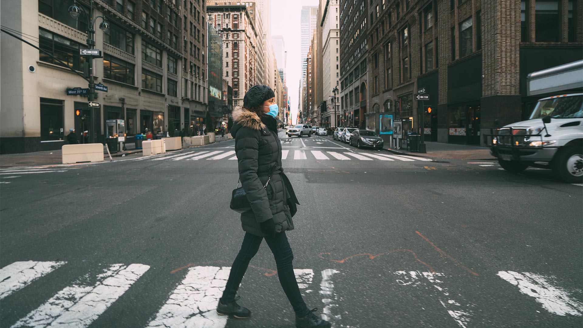 woman crossing a wide New York street wearing a mask 