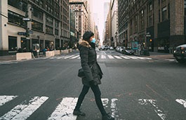 woman crossing a wide New York street wearing a mask 