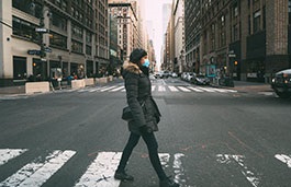 woman crossing a wide New York street wearing a mask