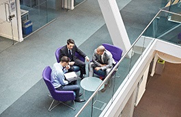 Down facing view of a group of three men wearing suits having a conversation at a table 