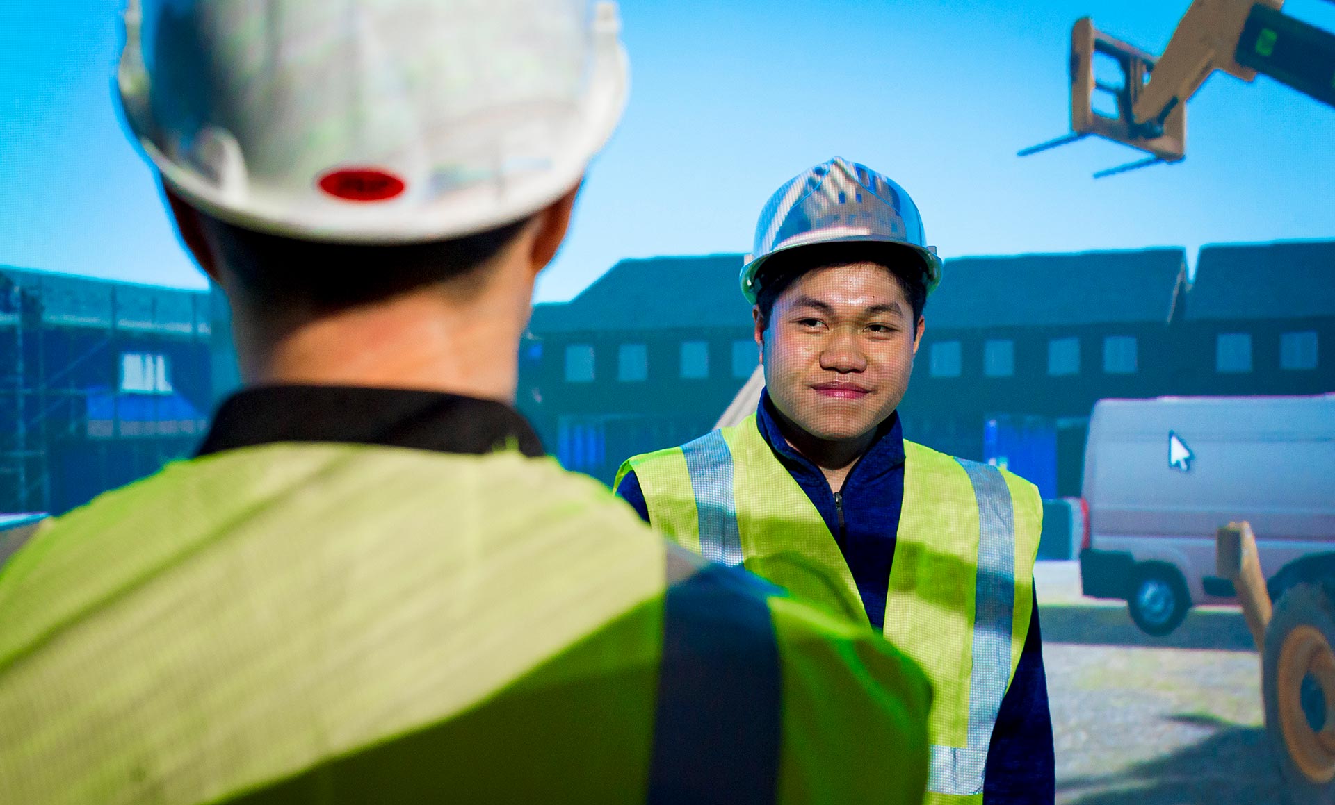 Two people at work talking to each other wearing fluorescent jackets and helmets