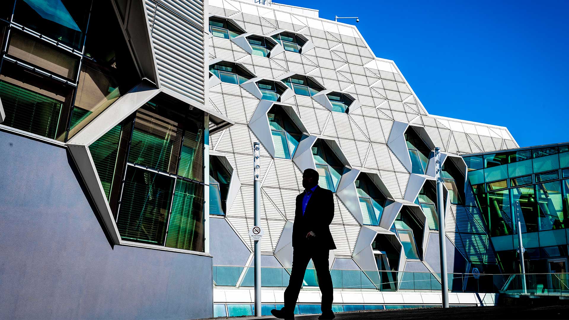 A silhouetted person walking past a modern architecture building wearing a suit