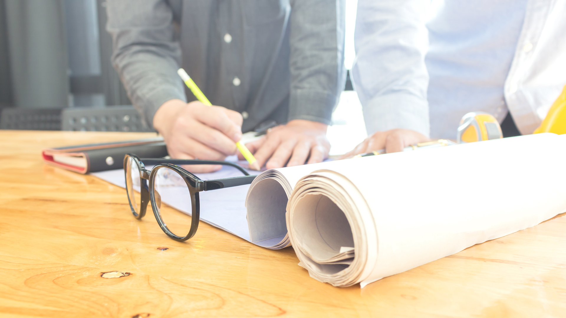 Close up of hands working on paperwork on a table with glasses and rolls of paper in the foreground