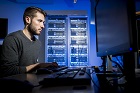 A male student concentrating on his computer screen in a dark blue lit room