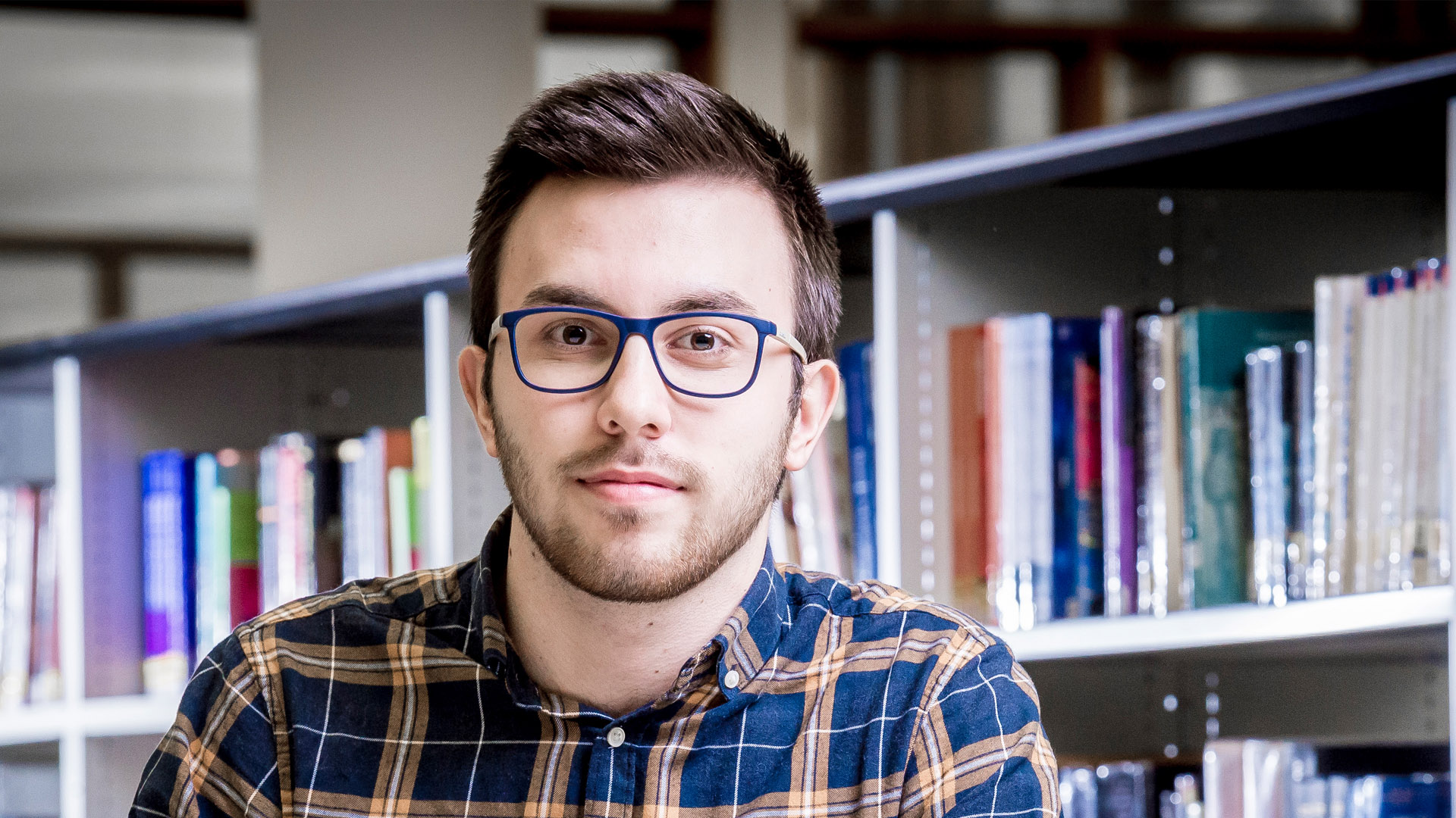 Male student sat in front of shelf of books