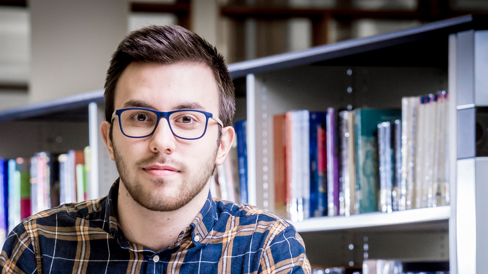 male student sitting in front of a shelf of books