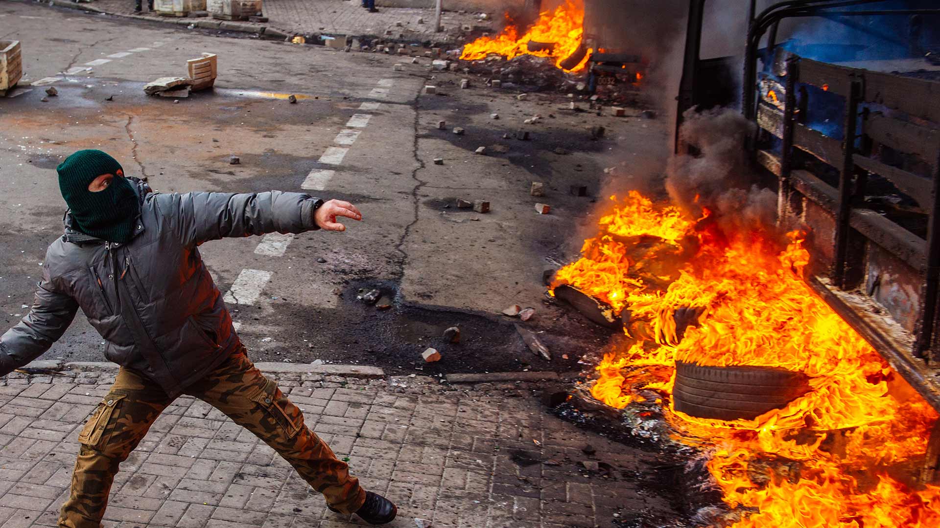 Man protesting in front of a burning wall