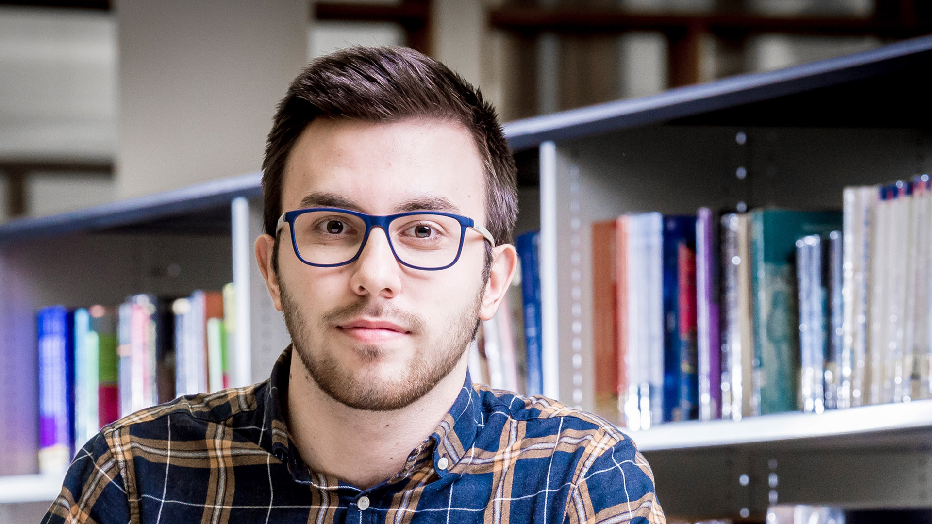 Male student sat in front of a shelf of books
