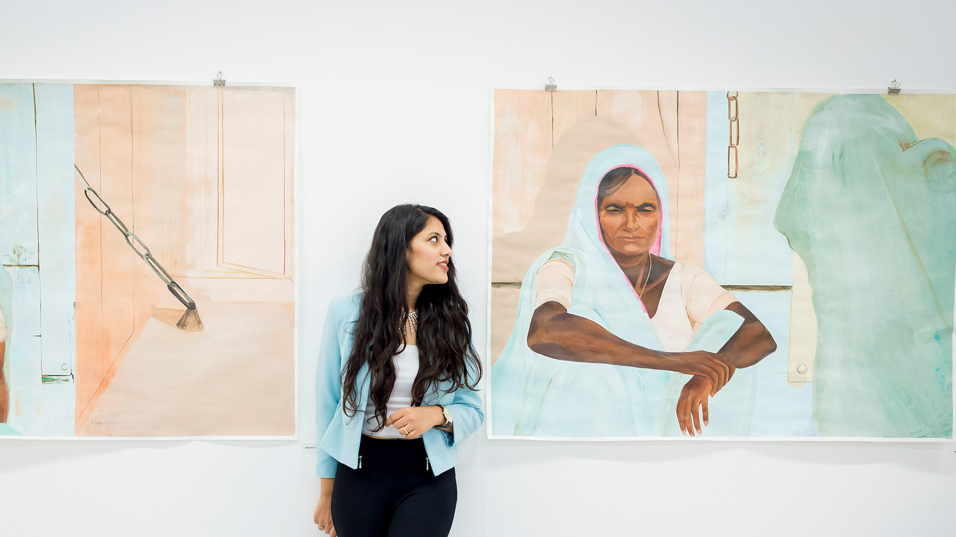 student leaning against a gallery wall with paintings on it