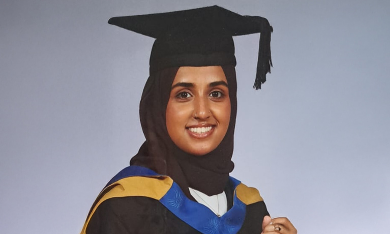 Zainab Ahmed smiling in a graduation cap and gown infront of a plain background