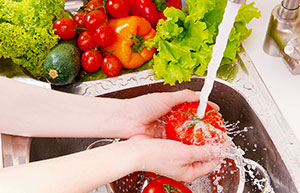 Arms and hands washing a vegetable in a sink with the tap running and other vegetables in the side