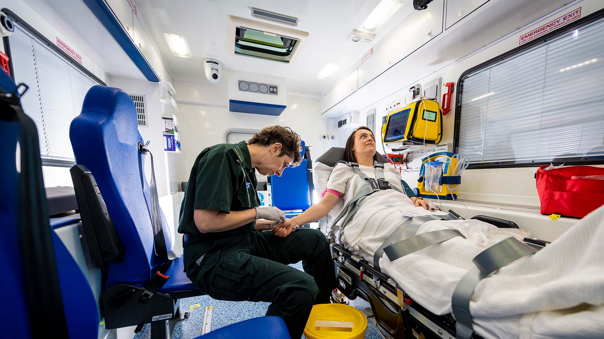 Man putting a cannula in a ladies arm in an ambulance