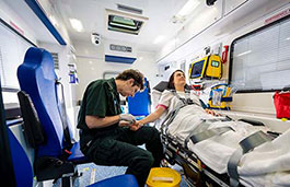 Man putting a cannula in a ladies arm in an ambulance