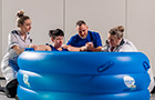 A woman giving birth in a blue water bath with two nurses either side and a visitor behind her for support