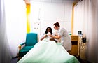 Young nurse comforting a young lady sitting in a hospital bed