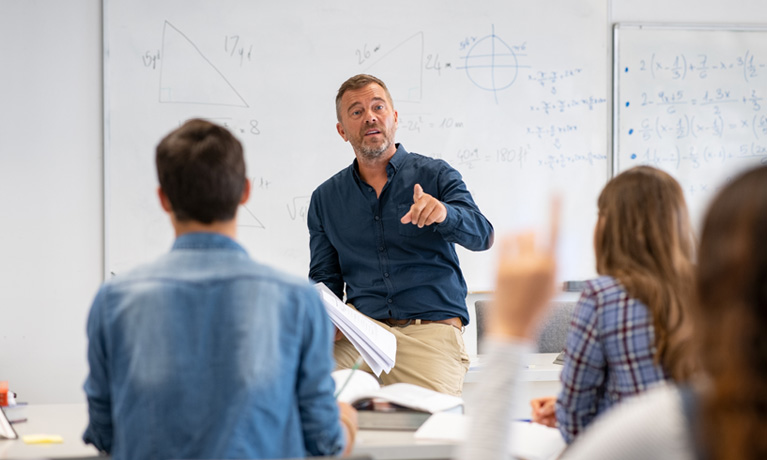 Teacher at the front of a clasroom with students sat at desks, learning